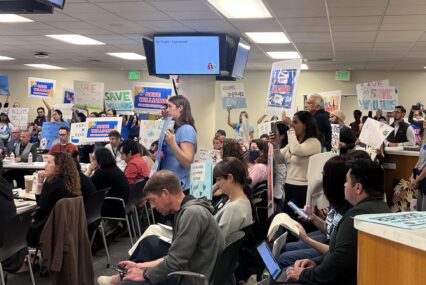People holding up protest signs at a school board meeting in San Jose, California
