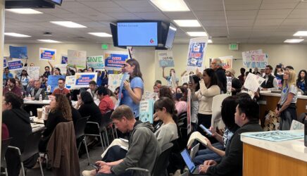 People holding up protest signs at a school board meeting in San Jose, California