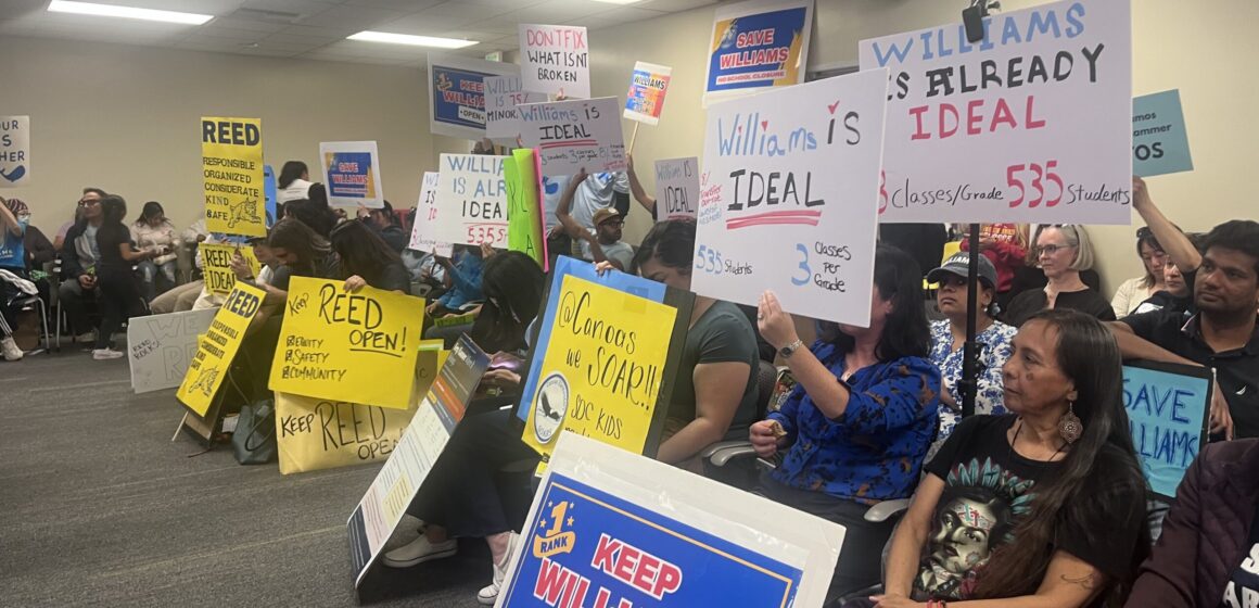 Personas sentadas en sillas con carteles de protesta en una reunión de la junta escolar en San José, California.