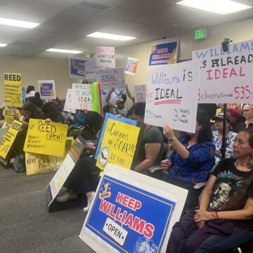 People sitting in chairs holding protest signs at a school board meeting in San Jose, California