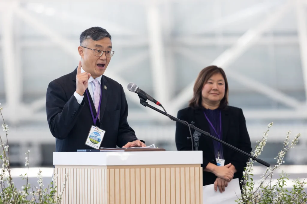 A man speaking at a podium with a woman standing slightly behind him