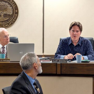 Two men up on a dais at a government meeting, with another man in front of them in Campbell, California