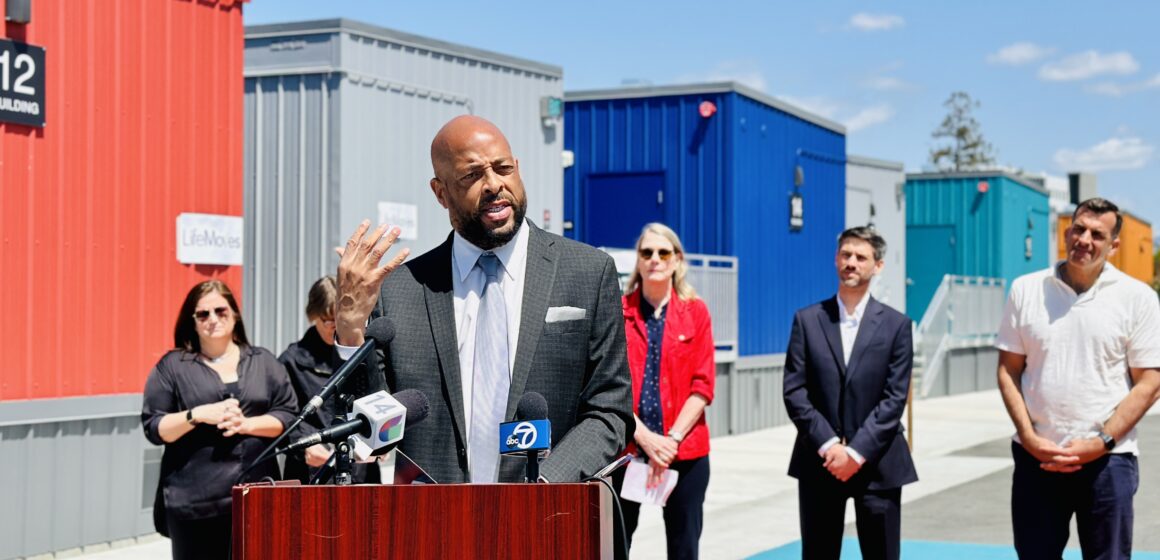 Aubrey Merriman LifeMoves A man speaking at a podium outside, with other people standing behind him