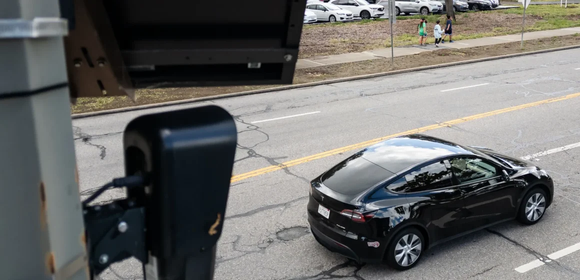 An automated license plate reader on a pole overlooking a car driving in Palo Alto, California
