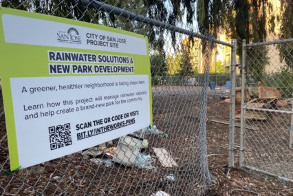 A metal chain-link fence in front of a park area.