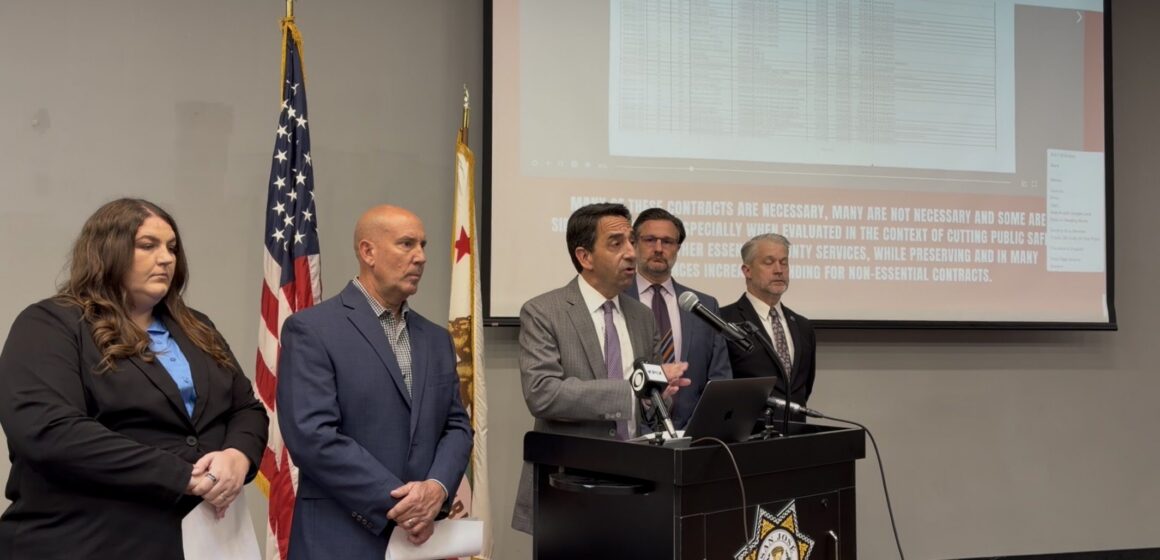 A man speaks at a podium, with other people standing next to him