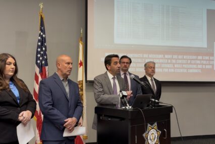 A man speaks at a podium, with other people standing next to him