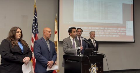 A man speaks at a podium, with other people standing next to him