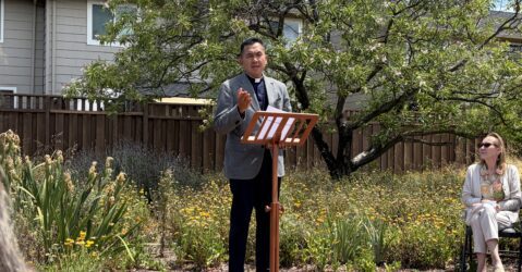 A man stands at a podium outside leading a prayer