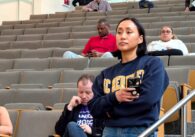 A woman holding a phone waiting to speak at a public meeting