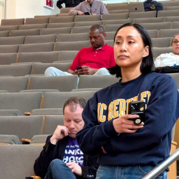 A woman holding a phone waiting to speak at a public meeting