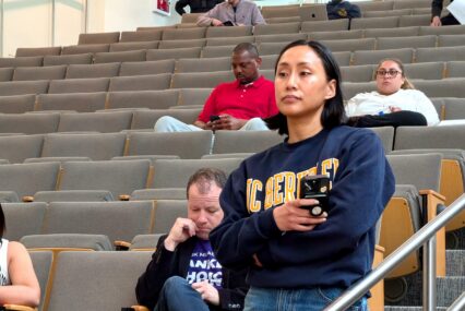 A woman holding a phone waiting to speak at a public meeting