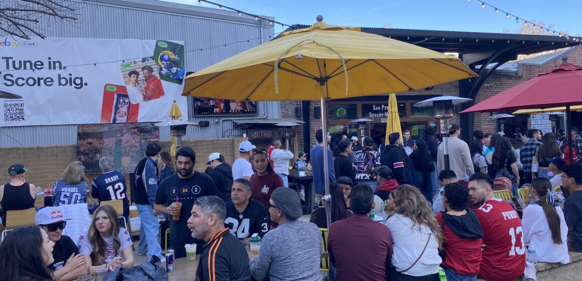 Super Bowl 60 watch party People sit underneath a yellow umbrella in an outdoor patio