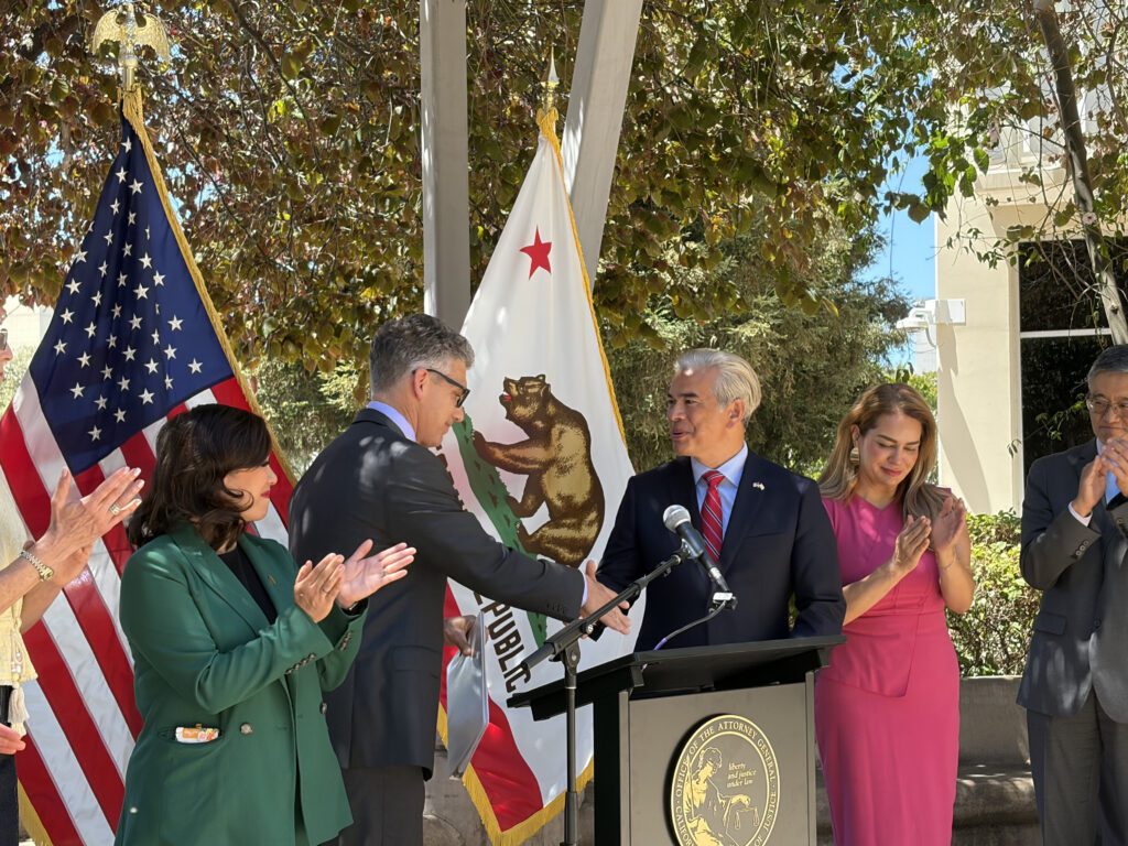 Two men shaking hands at a podium at a government press conference in San Jose, California