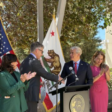Two men shaking hands at a podium at a government press conference in San Jose, California