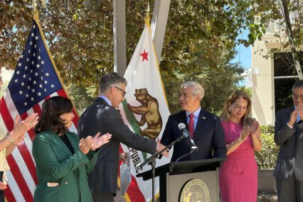 Two men shaking hands at a podium at a government press conference in San Jose, California