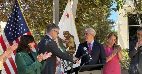 Two men shaking hands at a podium at a government press conference in San Jose, California