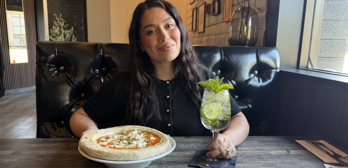 A woman sitting at a table in a restaurant with a pizza and drink