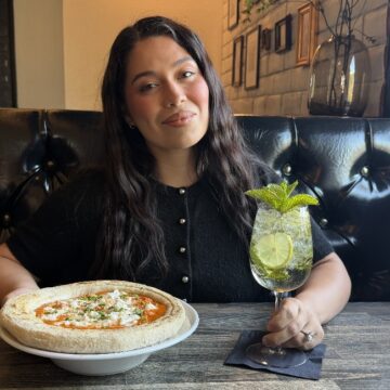A woman sitting at a table in a restaurant with a pizza and drink