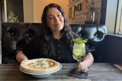 A woman sitting at a table in a restaurant with a pizza and drink