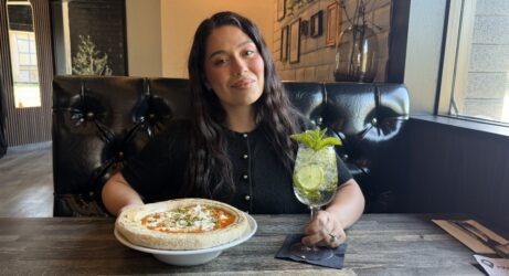 A woman sitting at a table in a restaurant with a pizza and drink