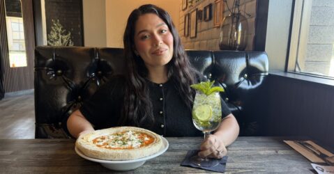 A woman sitting at a table in a restaurant with a pizza and drink