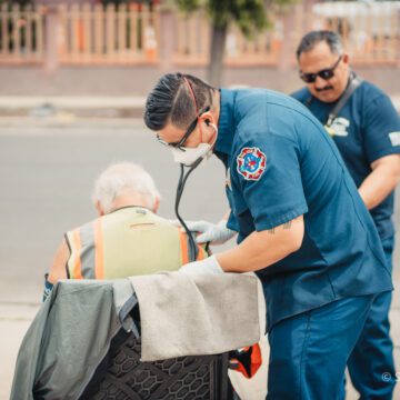 Firefighter paramedics Two paramedics in blue stand next to a man in a chair.