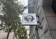 Un cartel en un edificio de piedra junto a unos árboles.