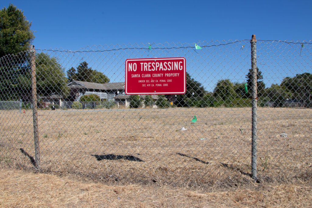 A chain link fence with a no trespassing sign in front of a vacant piece of land in Santa Clara, California