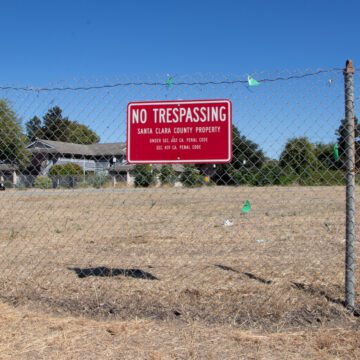 A chain link fence with a no trespassing sign in front of a vacant piece of land in Santa Clara, California
