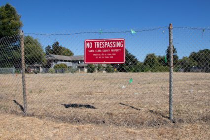 A chain link fence with a no trespassing sign in front of a vacant piece of land in Santa Clara, California