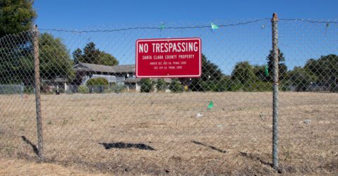 A chain link fence with a no trespassing sign in front of a vacant piece of land in Santa Clara, California
