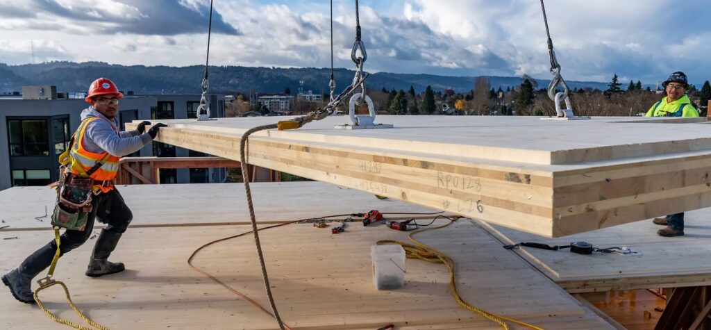 Construction workers handling mass timber being lifted by a crane