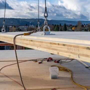 Madera en masa Trabajadores de la construcción manipulan madera maciza que está siendo izada por una grúa.
