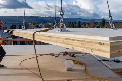 Construction workers handling mass timber being lifted by a crane