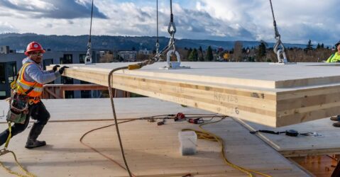 Construction workers handling mass timber being lifted by a crane
