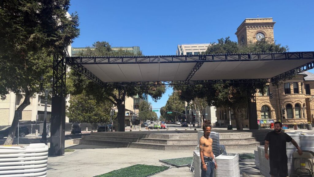 Two men standing in a plaza with stacks of plastic chairs in San Jose, California
