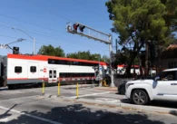 A train passes through a crossing while cars wait behind a striped barrier in Palo Alto, California