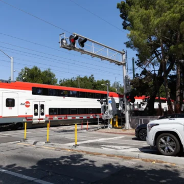 Cruce de Caltrain de Palo Alto en Embarcadero Un tren pasa por un cruce mientras los coches esperan detrás de una barrera a rayas en Palo Alto, California.