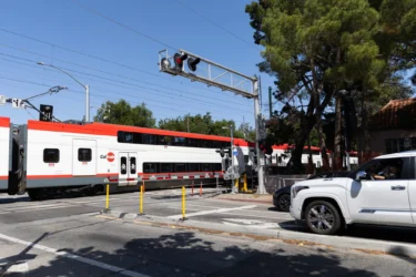 Palo Alto Caltrain crossing Embarcadero A train passes through a crossing while cars wait behind a striped barrier in Palo Alto, California