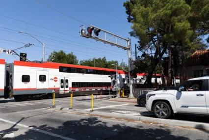 A train passes through a crossing while cars wait behind a striped barrier in Palo Alto, California