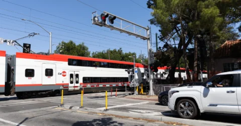 A train passes through a crossing while cars wait behind a striped barrier in Palo Alto, California