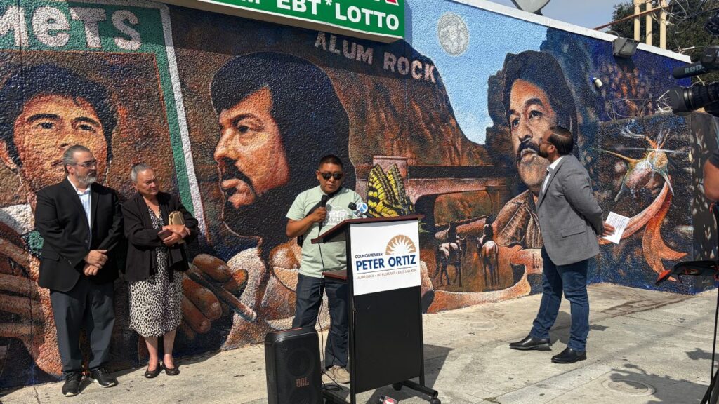 People at a podium standing in front of a mural in San Jose, California