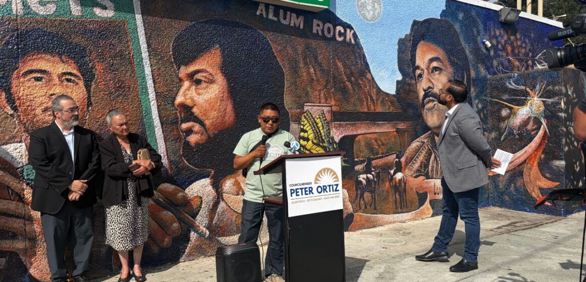 People at a podium standing in front of a mural in San Jose, California