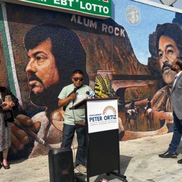 People at a podium standing in front of a mural in San Jose, California