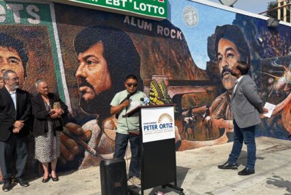 People at a podium standing in front of a mural in San Jose, California