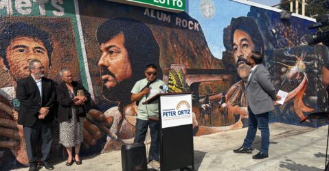 People at a podium standing in front of a mural in San Jose, California