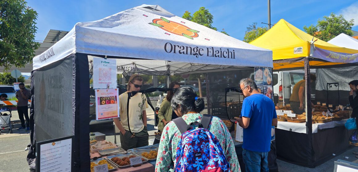Orange Elaichi Stall People getting food from a pop-up stand at a farmers market in Cupertino, California