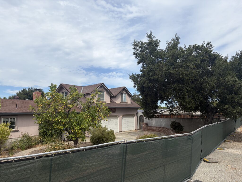 A house and a tree behind a green fence.