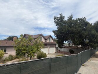 A house and a tree behind a green fence.